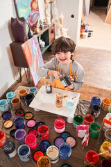 Boy laughing out loud while holding jar with paints and preparing creating his own masterpiece