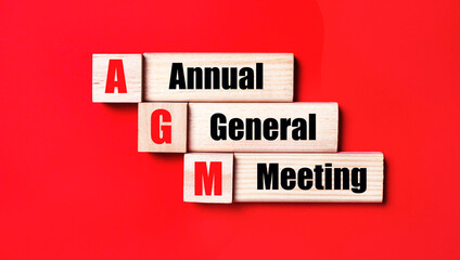 On a bright red background, wooden cubes and blocks with the text AGM Annual General Meeting....