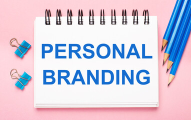 On a light pink background, light blue pencils, paper clips and a white notebook with the text PERSONAL BRANDING