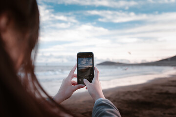 Chica sacando fotografías con el móvil en una playa de Islas Canarias