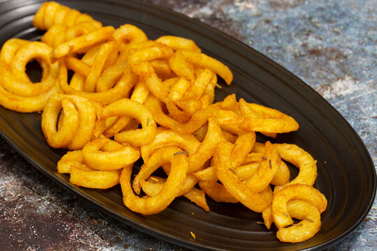 Spicy seasoned curly fries on a black stoneware oval plate.  Fast food concept