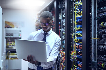 The man with the plan. Cropped shot of a IT technician working on his laptop while standing inside of a server room.