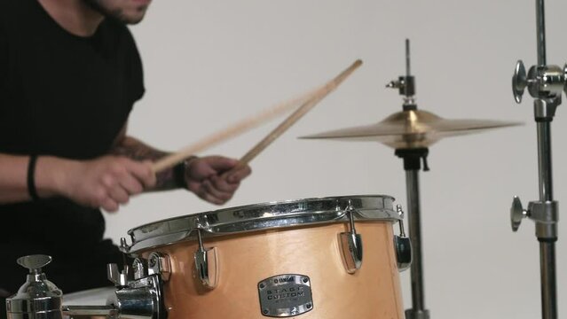 Caucasian guy with blue hair plays the drums. Yellow drum set. A drummer in black clothes plays on a white background. Close-up of a hi-hat.