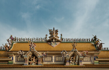 Bangkok, Thailand. Feb - 10, 2022 : Elaborate sculptures of monsters decorate on The Pariwas Ratchasongkram temple roof in blue sky background. Selective focus.
