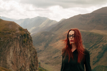 young woman in glasses stands on the background of mountains