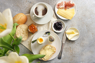 Continental breakfast with bread roll, cooked egg, jam, cheese, ham and coffee, light rustic...
