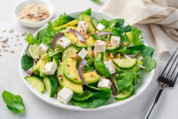 Salad with avocado close-up on a gray background. Vegetarian salad with vegetables, feta and seeds.