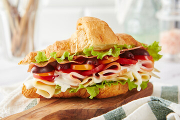 Croissant sandwich with cheese, ham, lettuce, tomatoes, olives and delicious sauce on wooden board.