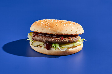 Beef burger blue background with hard shadow. American junk food minimal style. Hamburger trendy style.  Simple burger colour background.