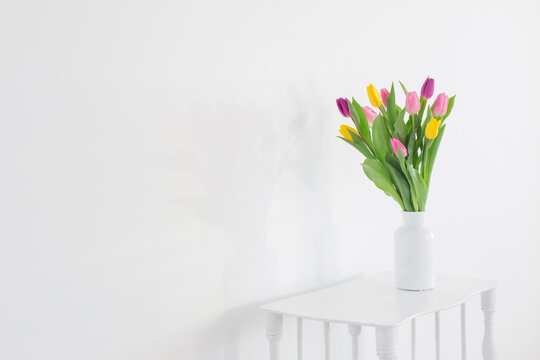 tulips in white vase on wooden shelf on white background
