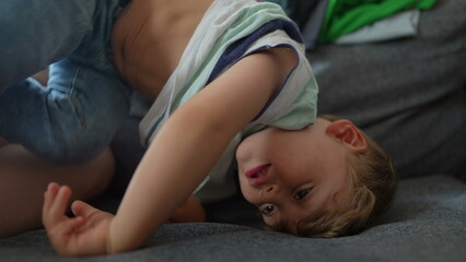 Bored little boy at home in upside down on sofa child playing alone