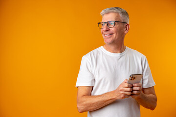 Senior smiling man using smartphone over yellow background