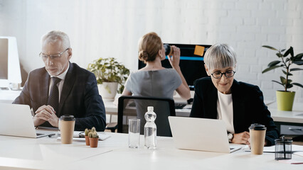 Smiling businesswoman looking at papers near coffee to go and laptop in office