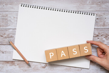 「PASS」と書かれた積み木、ペン、ノート、人の手