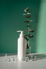 Eucalyptus and jars of cosmetics on a green background.