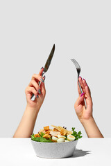 Caesar salad with croutons. A woman's hands with a knife and fork stick out from under the table. Creative
