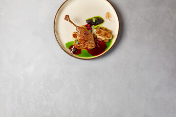 Duck confit with celery mash, cranberry and pear in handmade ceramic plate. Duck leg on modern dishware with hard shadow.