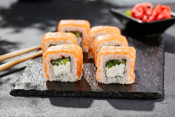 Maki sushi on dark stone table. Philadelphia maki with salmon. Sushi roll with cheese, cucumber inside, salmon outside. Style concept japanese menu with black background, leaves and hard shadow.