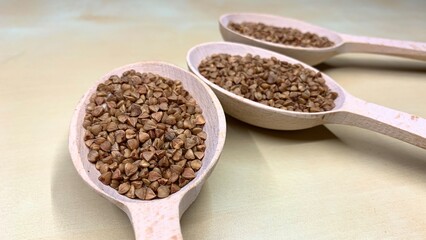 Buckwheat tea in a wooden spoon on a light wooden background. Buckwheat tea close-up macro photography. Scattered buckwheat tea pellets on wooden background