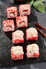 Maki sushi on dark slate.  Maki roll with crab topped. Sushi roll with crab, cream chees and tobika. Style concept japanese menu with black background, leaves and hard shadow.