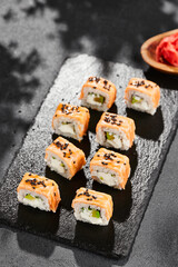 Maki sushi on dark slate. Hot philadelphia maki with baked salmon. Sushi roll with grilled salmon, cream cheese and avocado. Style concept japanese menu with black background, leaves and hard shadow.