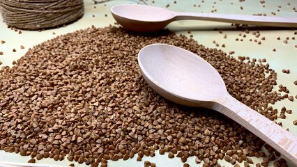 Buckwheat tea in a wooden spoon on a light wooden background. Buckwheat tea close-up macro photography. Scattered buckwheat tea pellets on wooden background
