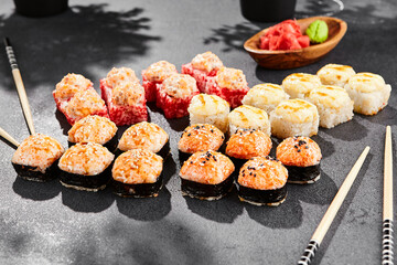 Hot maki set on dark slate. Baked sushi set with variety rolls. Sushi rolls with salmon,tobiko, crab and baked cheese topped. Style concept sushi menu with black background, leaves and hard shadow.