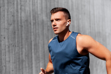 fitness, sport, training and lifestyle concept - young man in earphones running outdoors