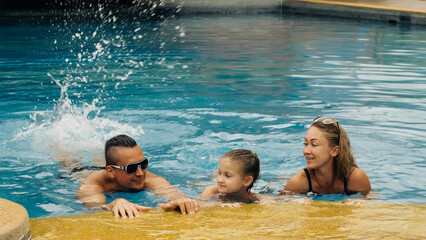 The mother and father with little daughter have fun in the pool. Mom and dad plays with the child....