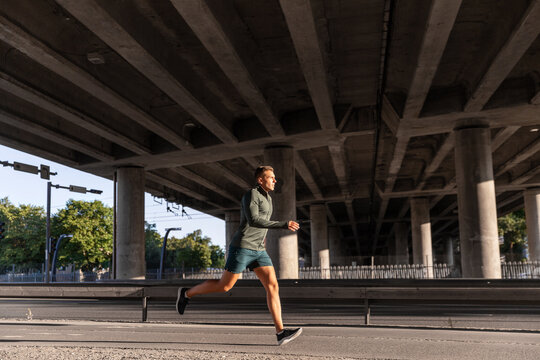 fitness, sport and healthy lifestyle concept - young man running outdoors under bridge