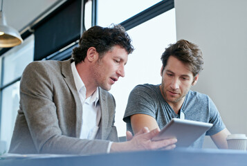 Technology and teamwork. Cropped shot of two businessmen working on a digital tablet.