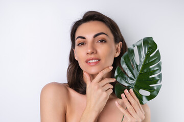 Close-up beauty portrait of a topless woman with perfect skin and natural make-up, with monstera palm leaf