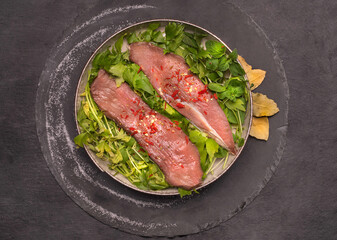 Raw pork tenderloin, sirloin and fresh herbs on a plate, on black background, top view. Cooking concept with raw meat.