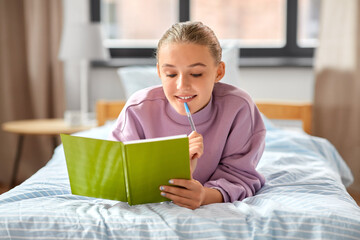 education, people and leisure concept - happy smiling thinking girl with diary lying on bed at home