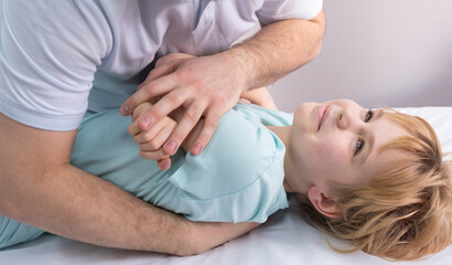 Obraz na płótnie Canvas An osteopath works with the child. Work with the chest, shoulders and spine. There is a teenage child on the couch. The doctor puts pressure on the patient's chest. Posture correction