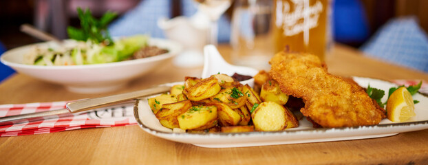 Saftiger Wiener Schnitzel vom Kalb mit wellen Panade und Bratkartoffeln auf schönem Teller 