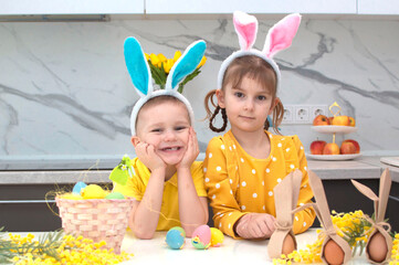 happy Easter! funny kids with bunny ears are getting ready for the holiday. A child, a boy and a girl, wear bunny ears and play with colorful eggs. Cheerful smiling children.