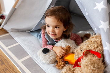 childhood, hygge and people concept - happy little baby girl playing with toys in kid's tent or teepee at home