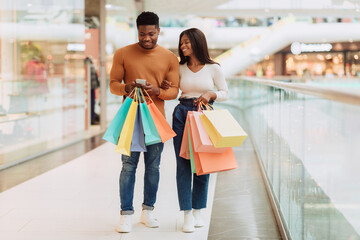 Happy black couple using phone walking with shopping bags