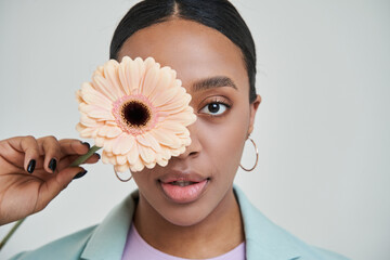 Brunette multiracial woman looking attentively and hiding her eye behind the flower