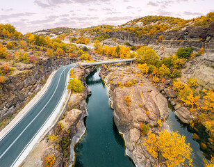 Aerial drone view of a road passing a narrow gorge of a river by bridge during golden autumn in Greece