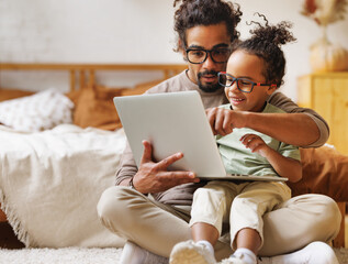 Happy african american family little son with dad watching funny videos on laptop together at home