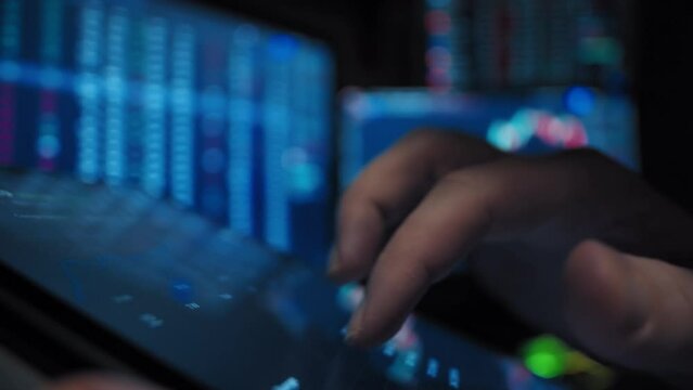 A man holds a tablet in hands looks and analyzes stock market graphics against the defocused background with market date close-up slow motion