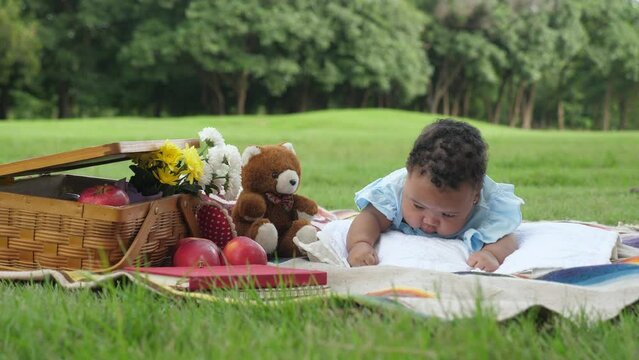 Low angle shot of a female African infant holding head up, bearing, trying to crawl and explore the environment around while picnicking at park