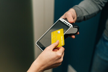 Close-up cropped shot of unrecognizable courier male giving POS wireless terminal to making contactless payment via credit card, to young female customer on doorway at home, top view.