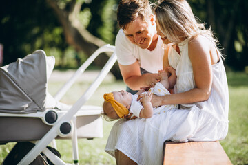 Young couple with their baby daughter in park sitting by ther baby carriage