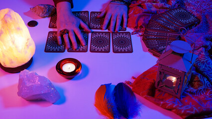Woman holding her hands above the lined up tarot cards. Tarot card reading session. Cyberpunk blue pink neon light. Predicting the future, esoteric, mystic.