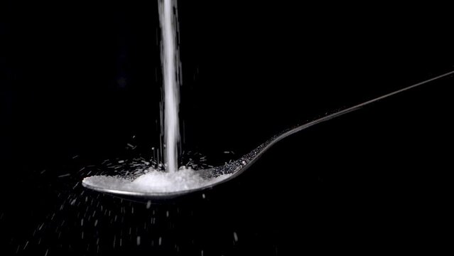 Unhealthy sugar falling and filling up a tablespoon, slow motion, isolated