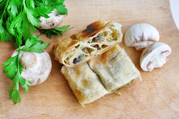 Homemade mushrooms pie.Fresh piece of savory strudel stuffed with  leek and mushrooms served on a wooden plate,with mushrooms and parsley