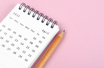 April 2022 desk calendar with wooden pencil on pink background.
